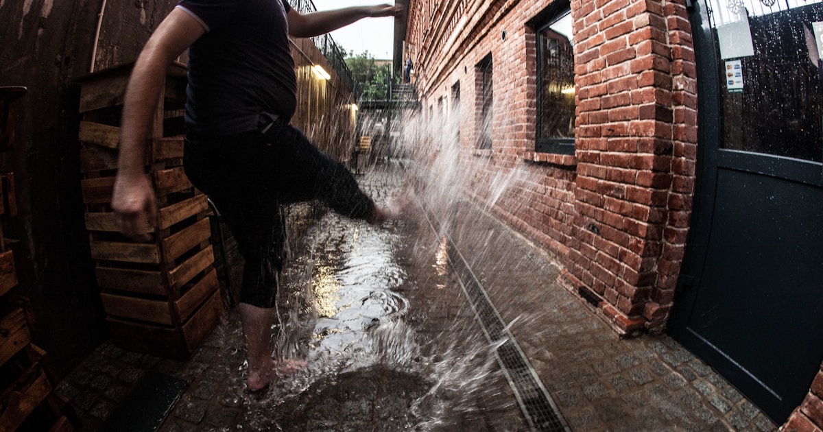 a man standing in a puddle of water next to a brick building