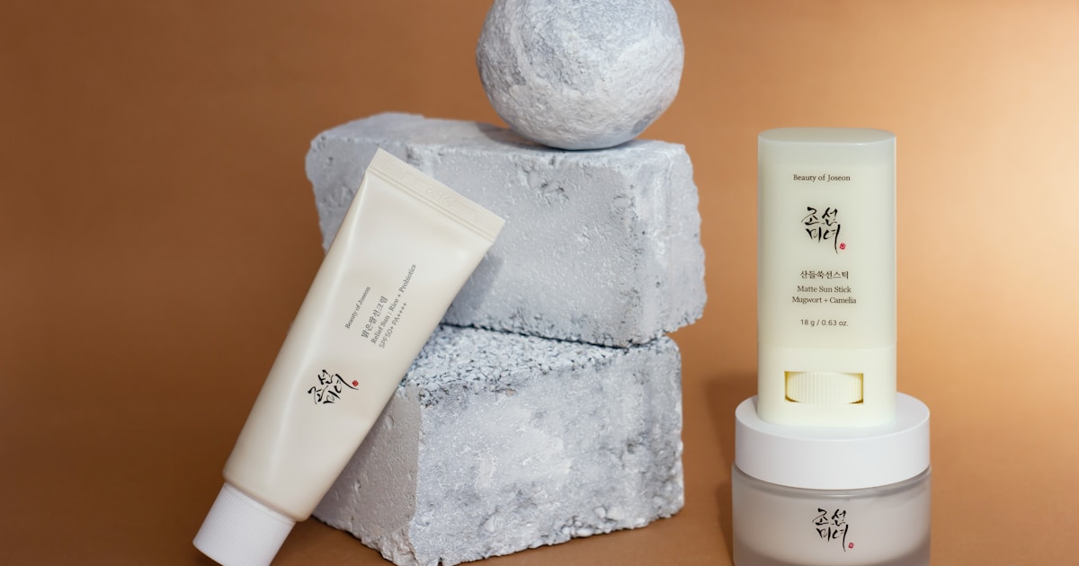 Two different sunscreens and a moisturizer from one K-brand make up a modern minimalist composition with rough pieces of painted concrete on a warm glowing background.