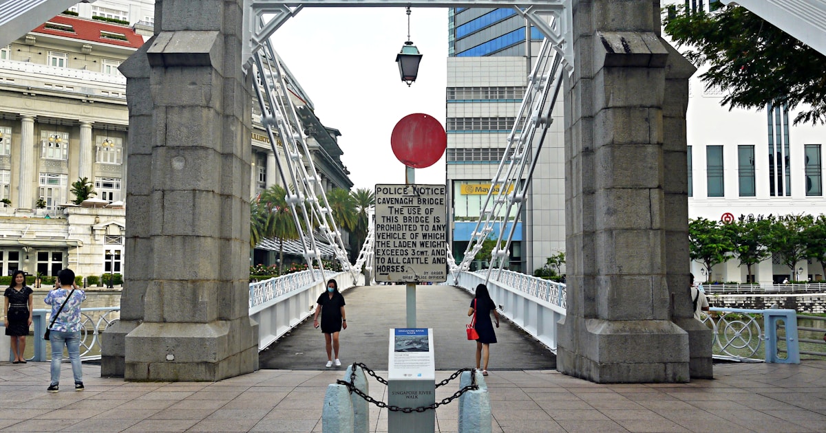 woman in white shirt and blue denim jeans standing on gray concrete bridge during daytime