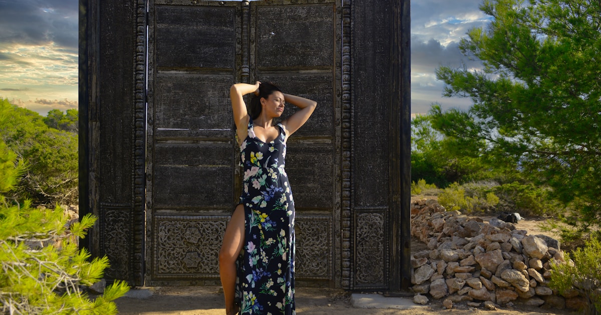 Woman in dress stands by rustic wooden structure