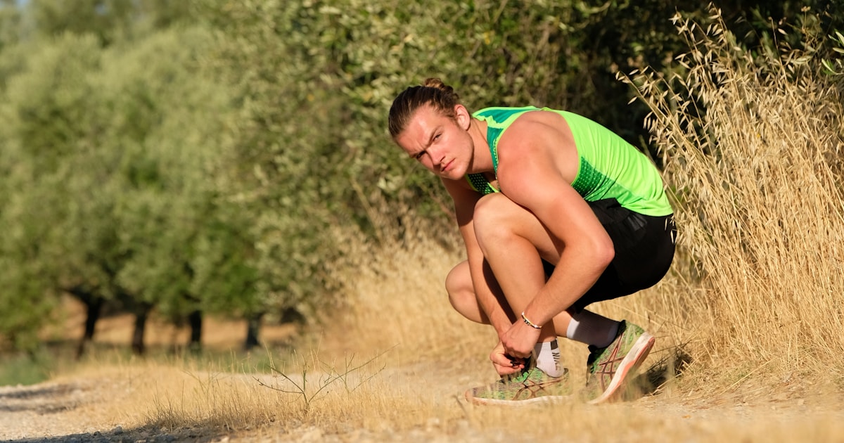 a man squatting down in a field with trees in the background